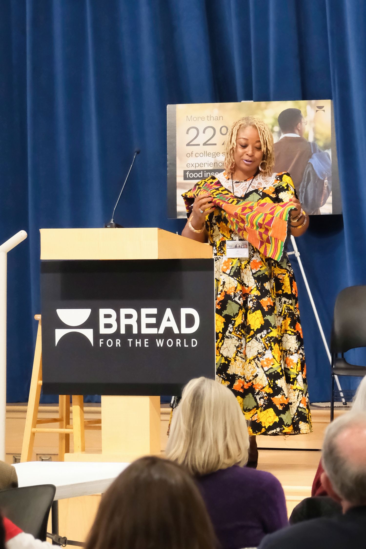 A speaker presents at a podium with the Bread for the World logo during an event with audience members visible.