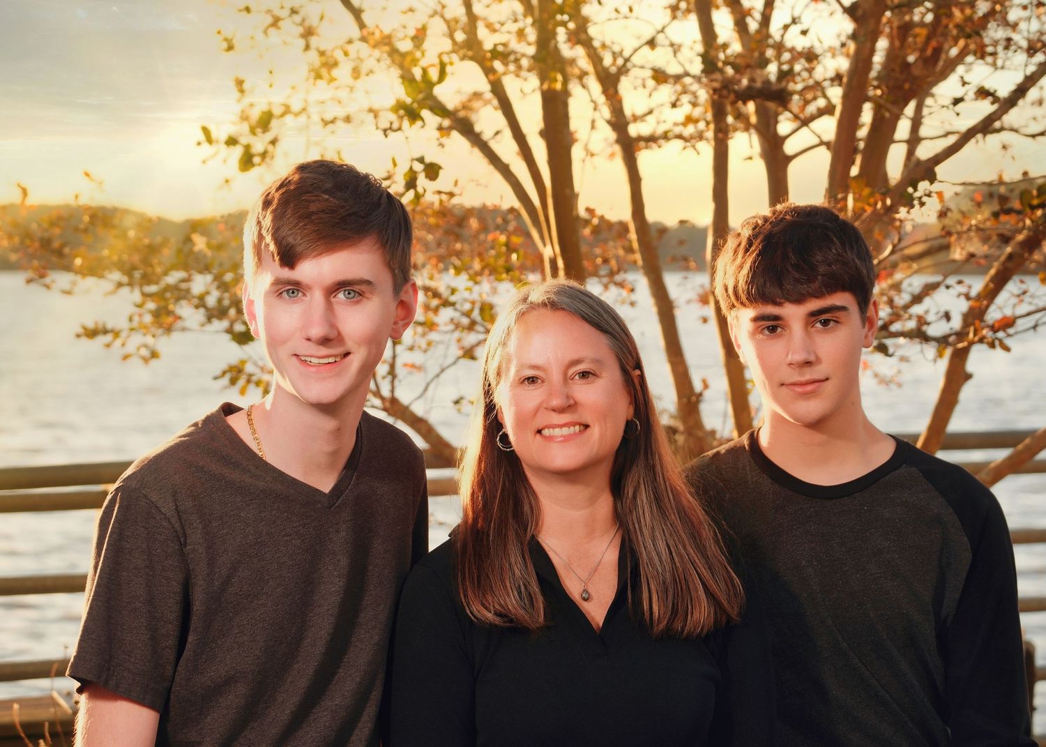 Three people posing together outdoors at sunset near water.