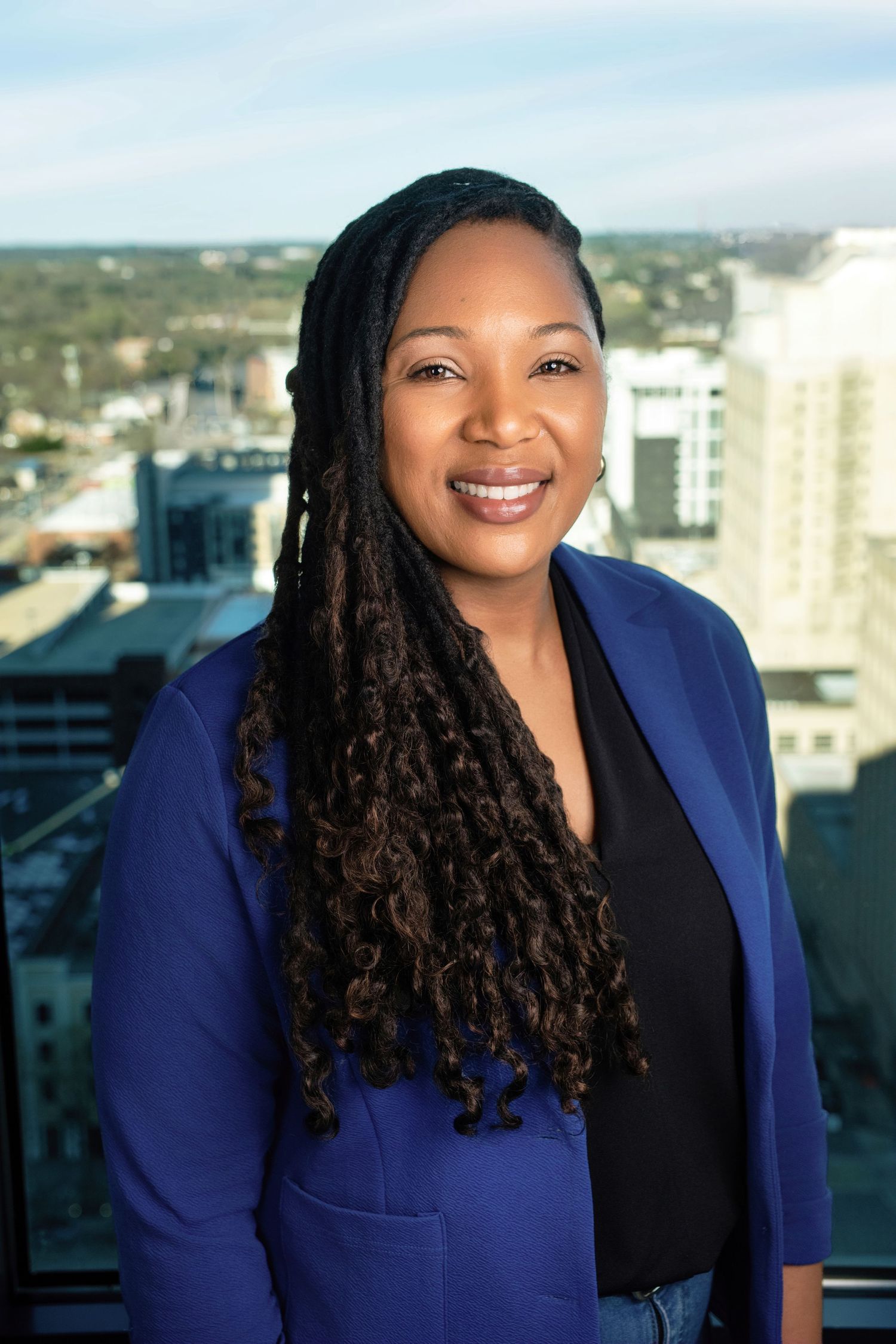 Professional portrait of person in navy blazer and black top against city skyline backdrop.
