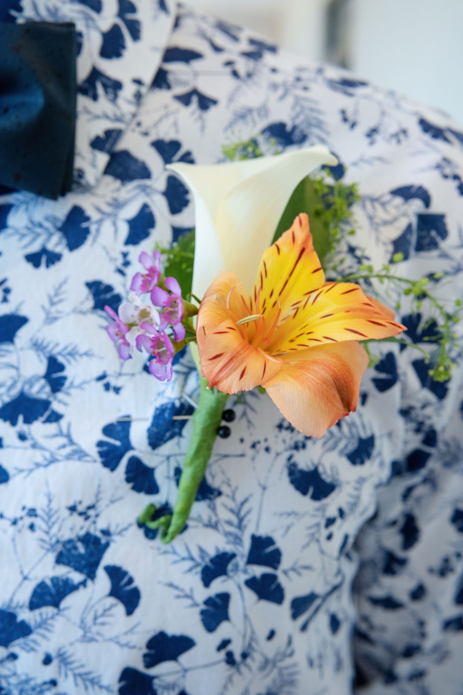 A peach-colored alstroemeria flower with small purple blooms rests against a blue and white patterned fabric background.