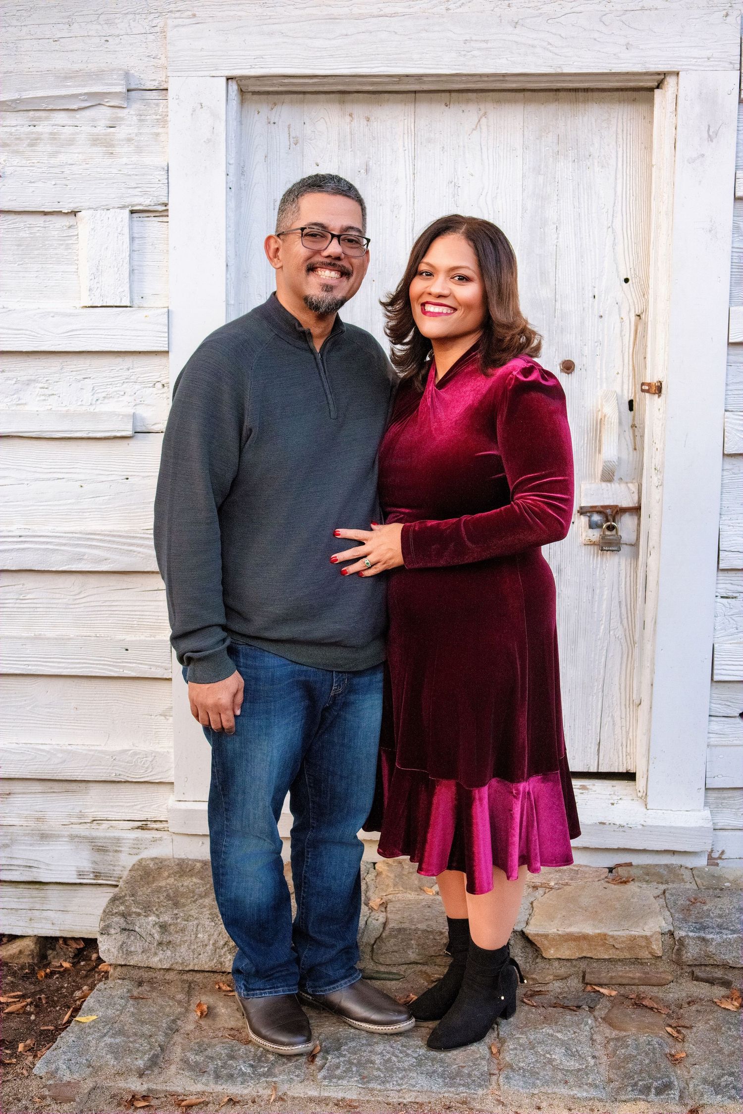 A couple in casual winter wear stands together in front of a white wooden door.