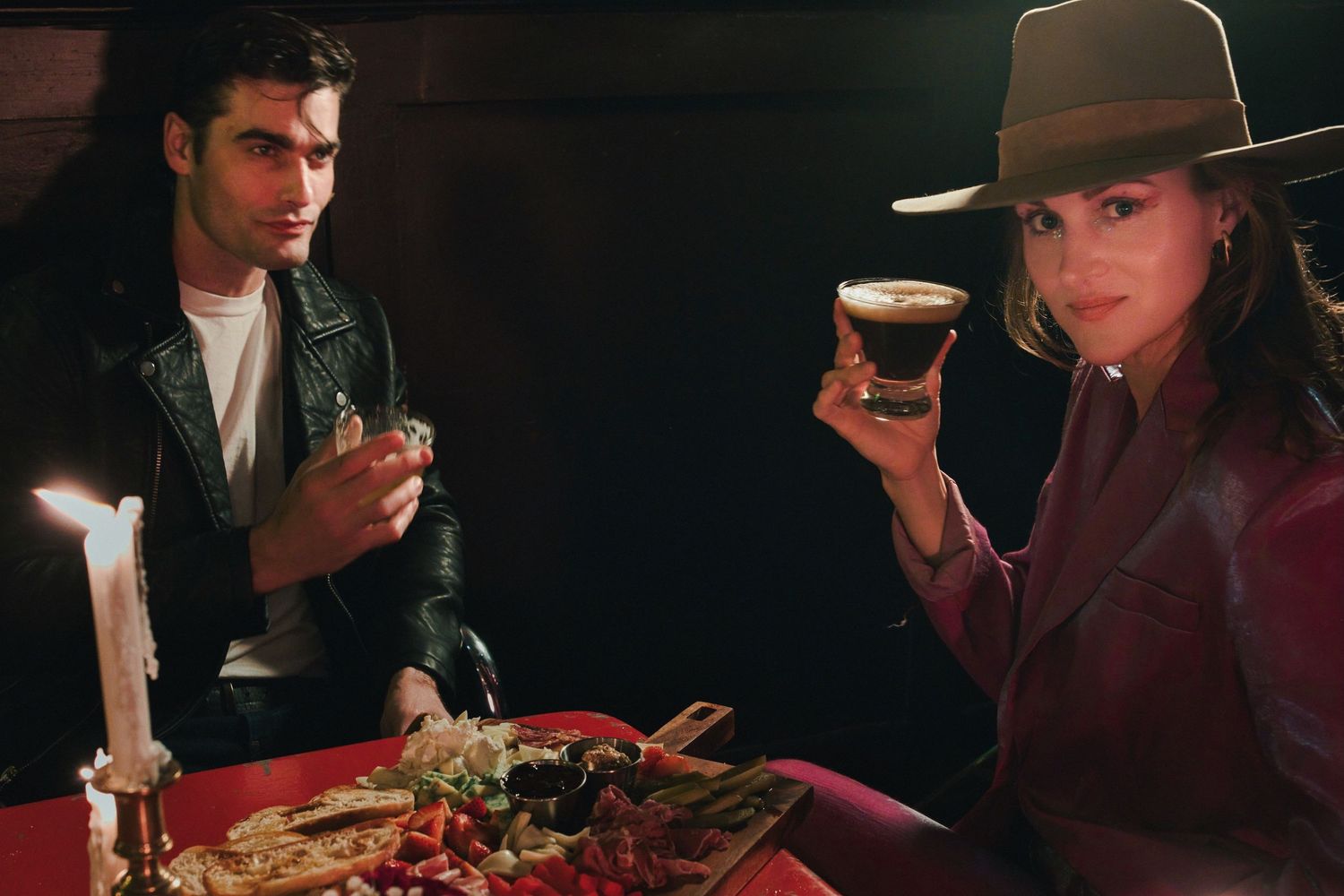 Two people enjoying drinks and food at a candlelit table in a dark restaurant.