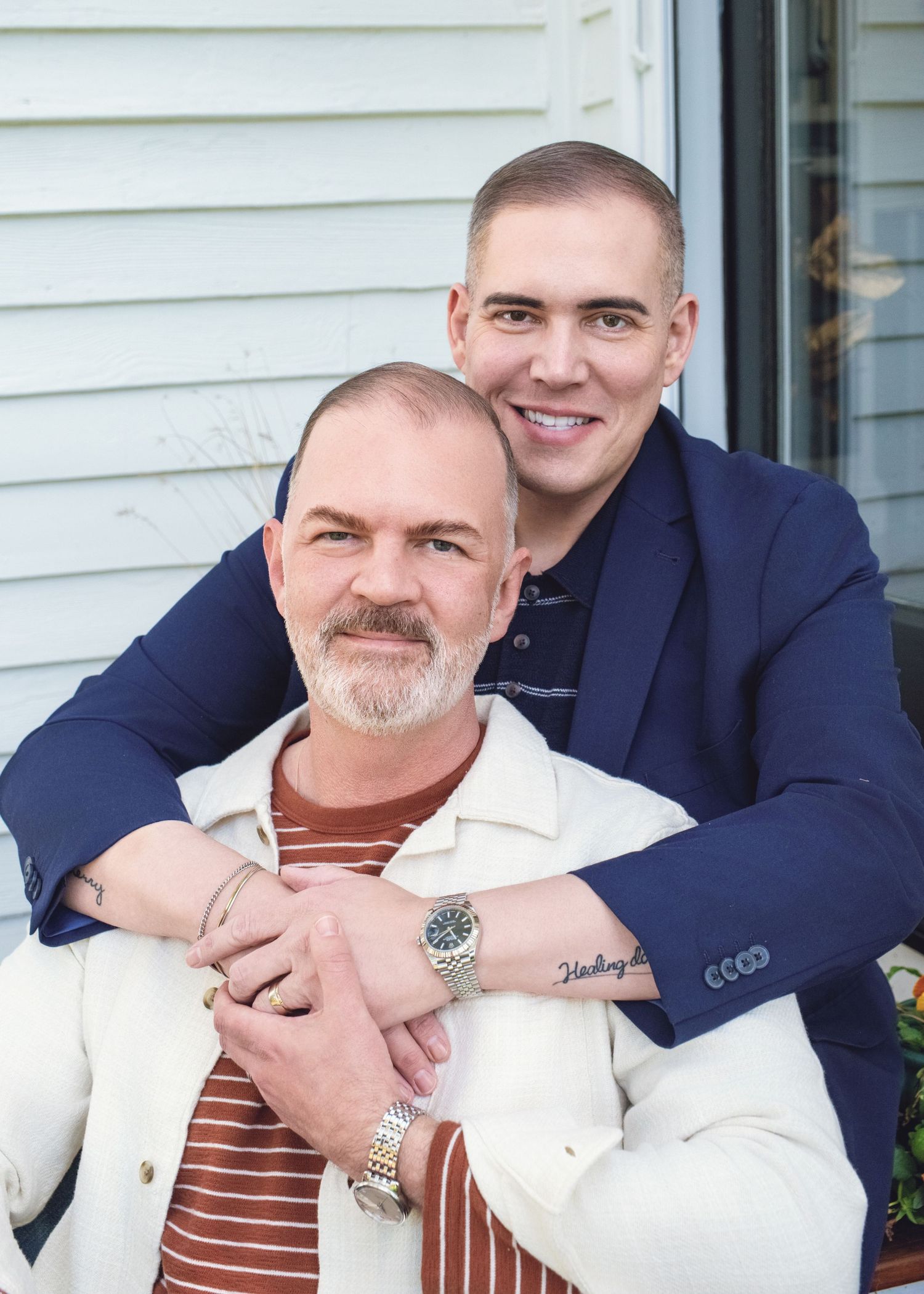 Two people pose together in a warm outdoor portrait while wearing a navy blazer and white jacket with stripe shirt.
