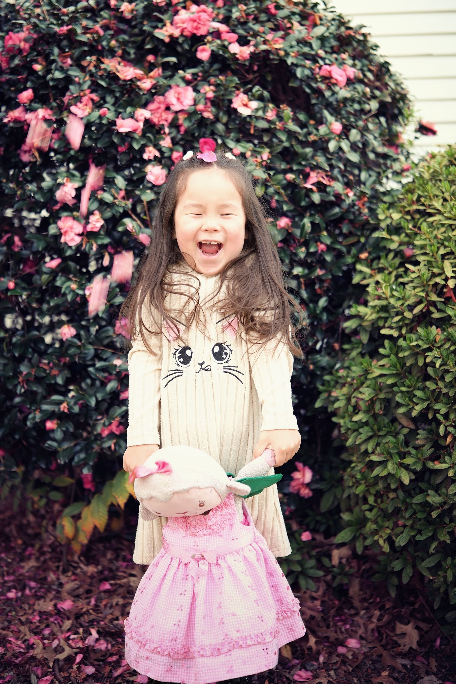 Joyful expression against pink flowering bushes wearing a cat-themed dress.