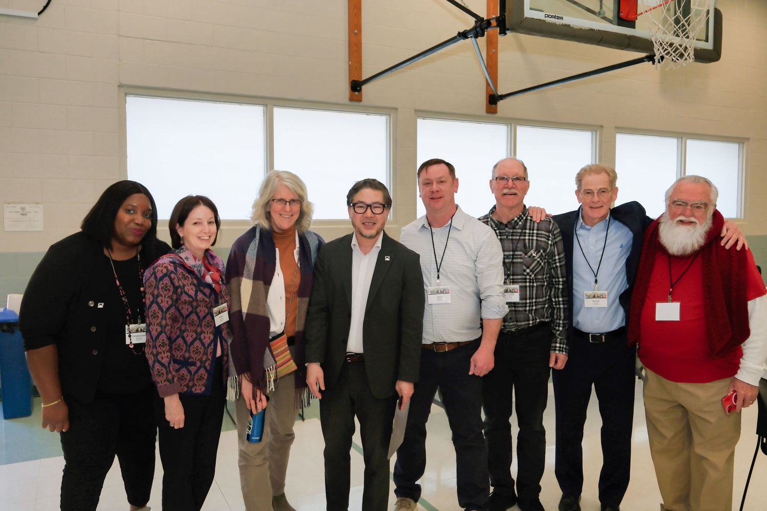 Group of educators and staff members standing together in a bright gym or multipurpose room with basketball hoop visible.