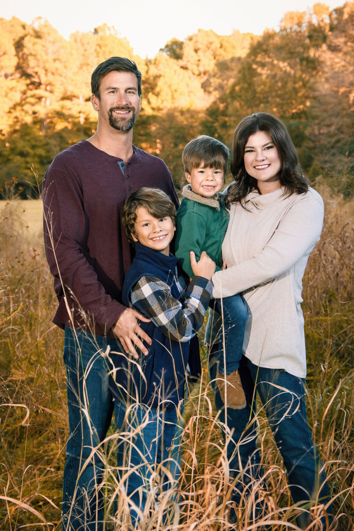 Family of four poses together in a golden field during sunset.