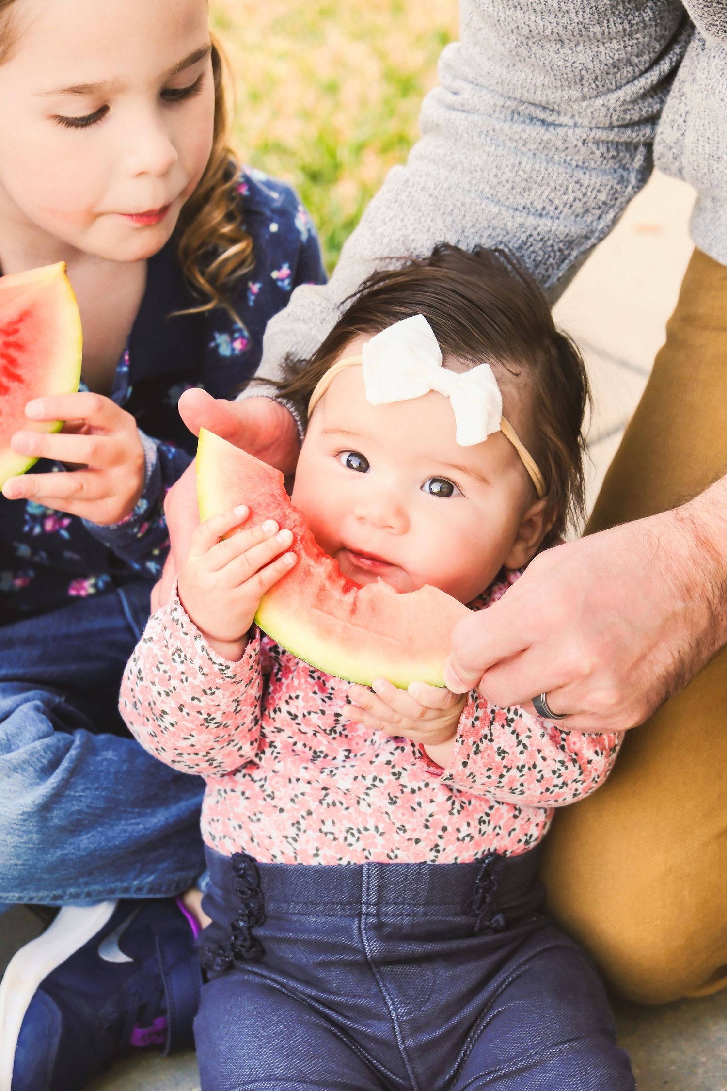A series of photos showing a baby in a floral top and jeans eating a slice of watermelon.