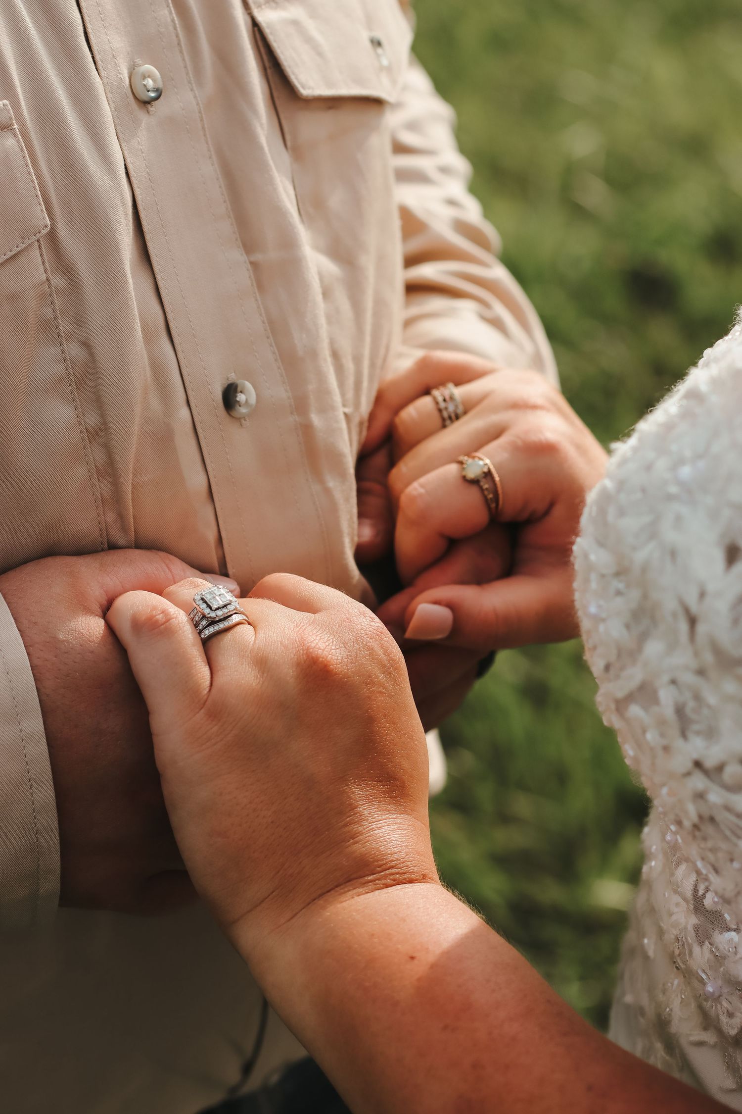 Bride and groom holding hands showing diamond wedding rings during outdoor ceremony.