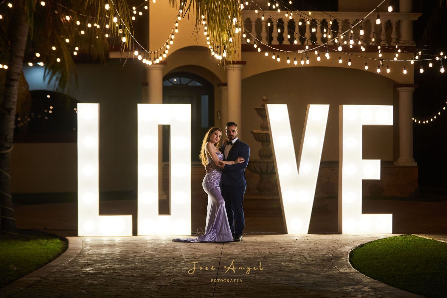 Illuminated LOVE marquee letters create a romantic backdrop for a nighttime wedding celebration.