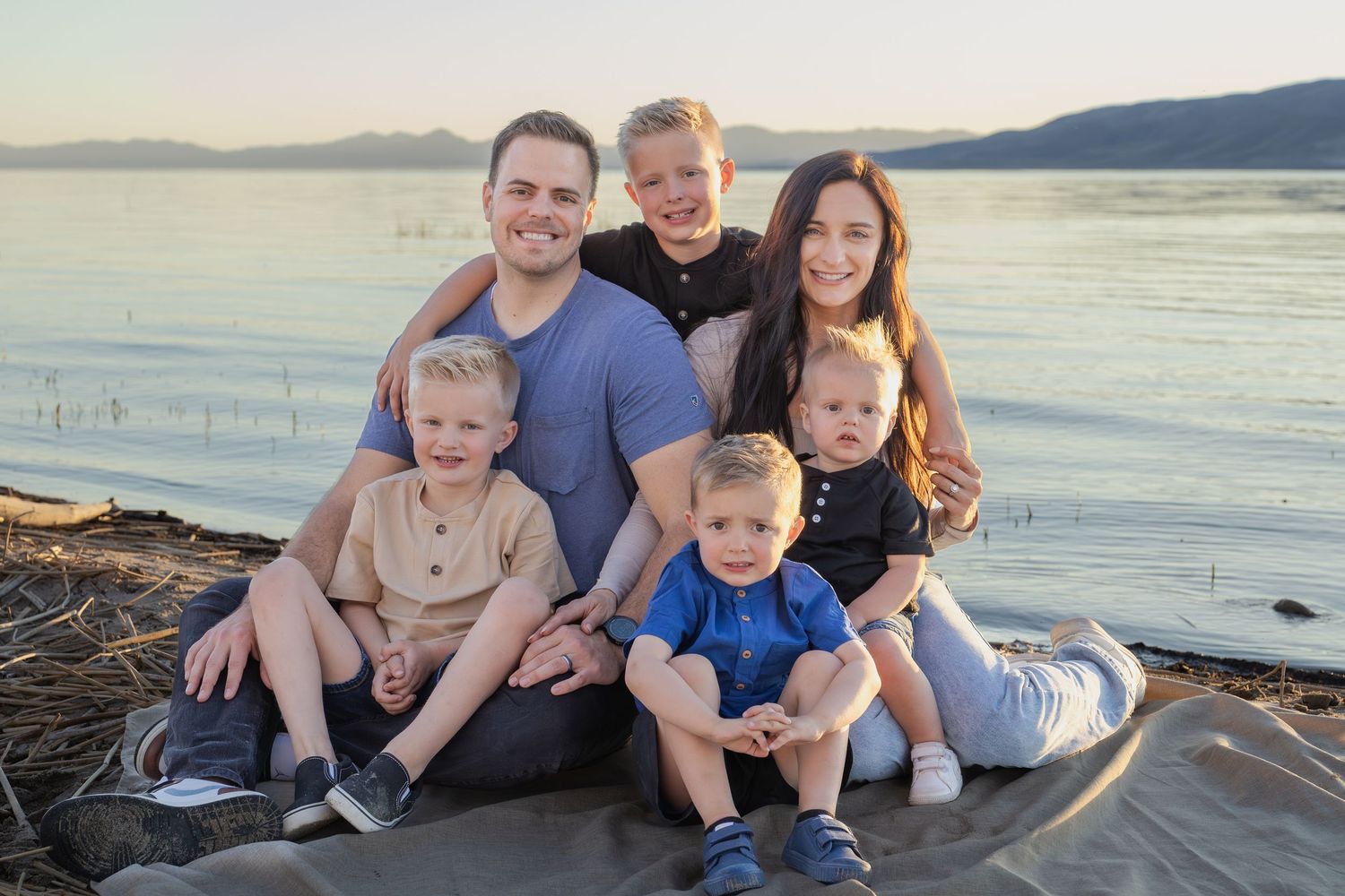 family with four boys taking photos at utah lake at sunset