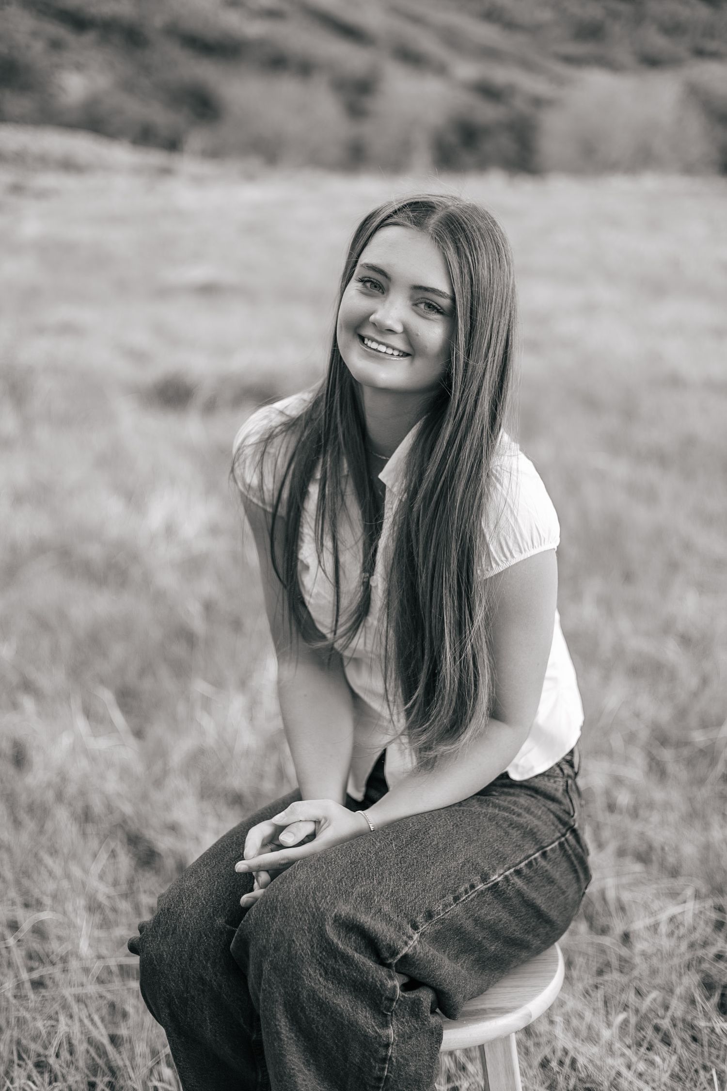 senior girl posing in a field, sitting on a stool