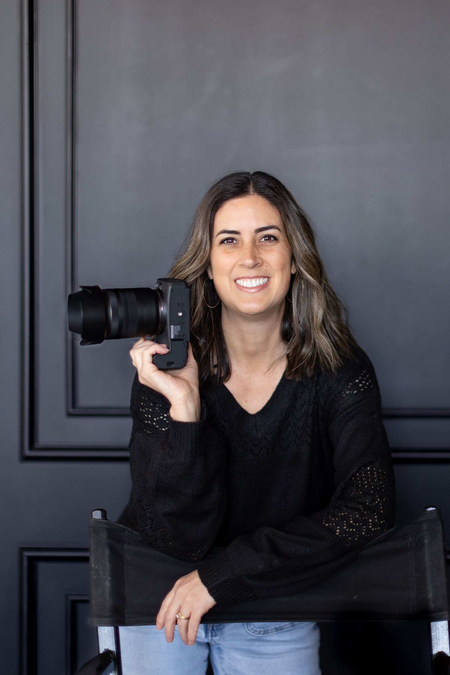 happy image of Sarah Rogers Photography with her camera, leaning on a director's chair in Utah photo studio