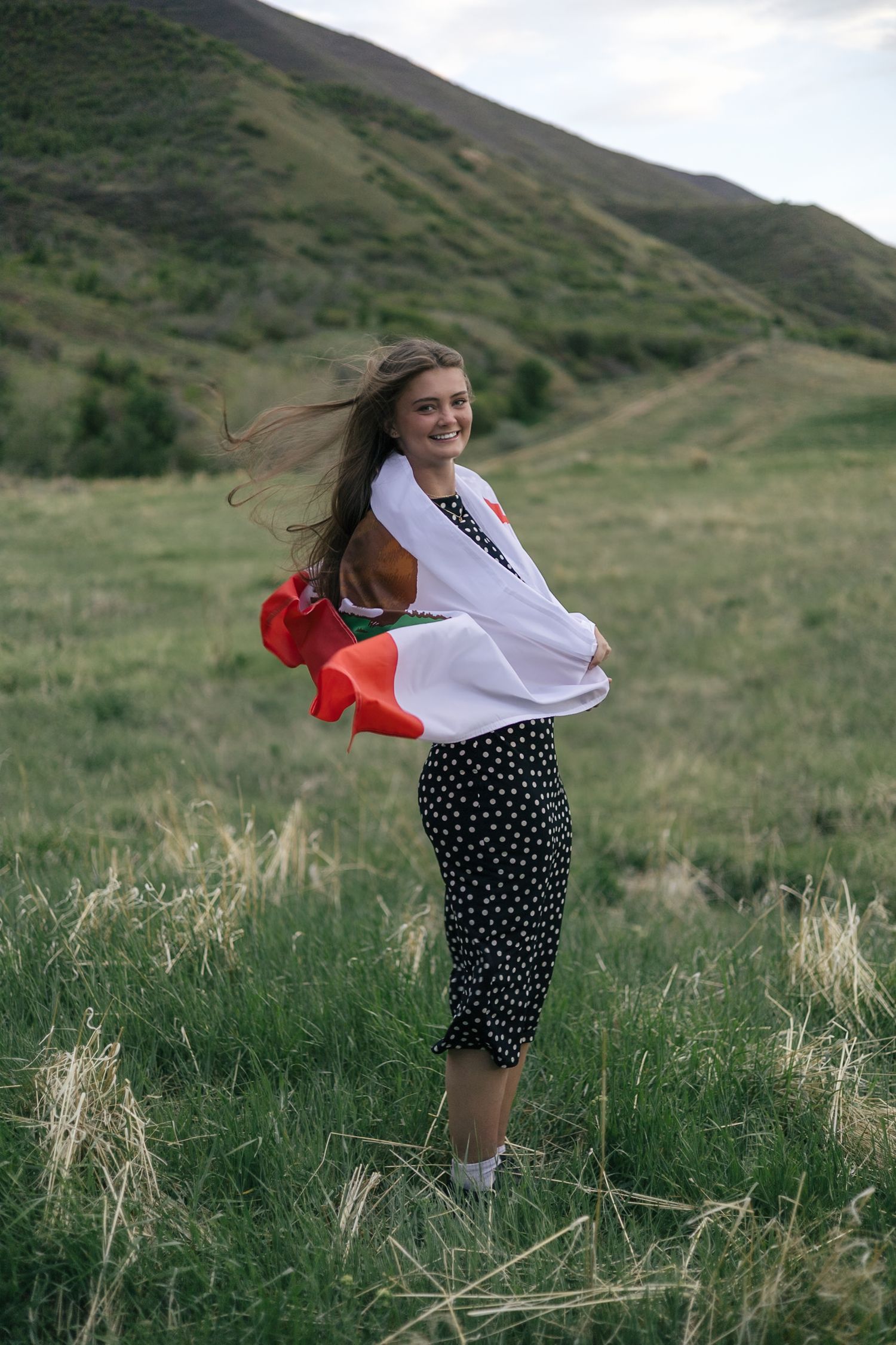 senior girl posing in a field, with california flag wrapped around her shoulders