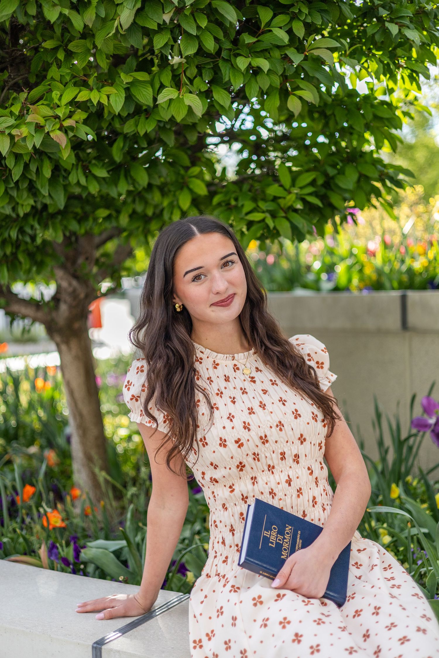 girl holding a book of scripture, leaning on her arm at an LDS temple garden