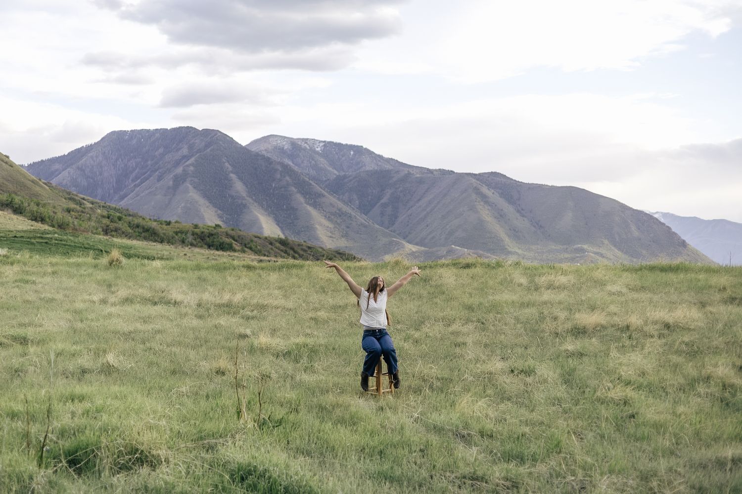 senior girl posing in a field, sitting on a stool and kicking her feet