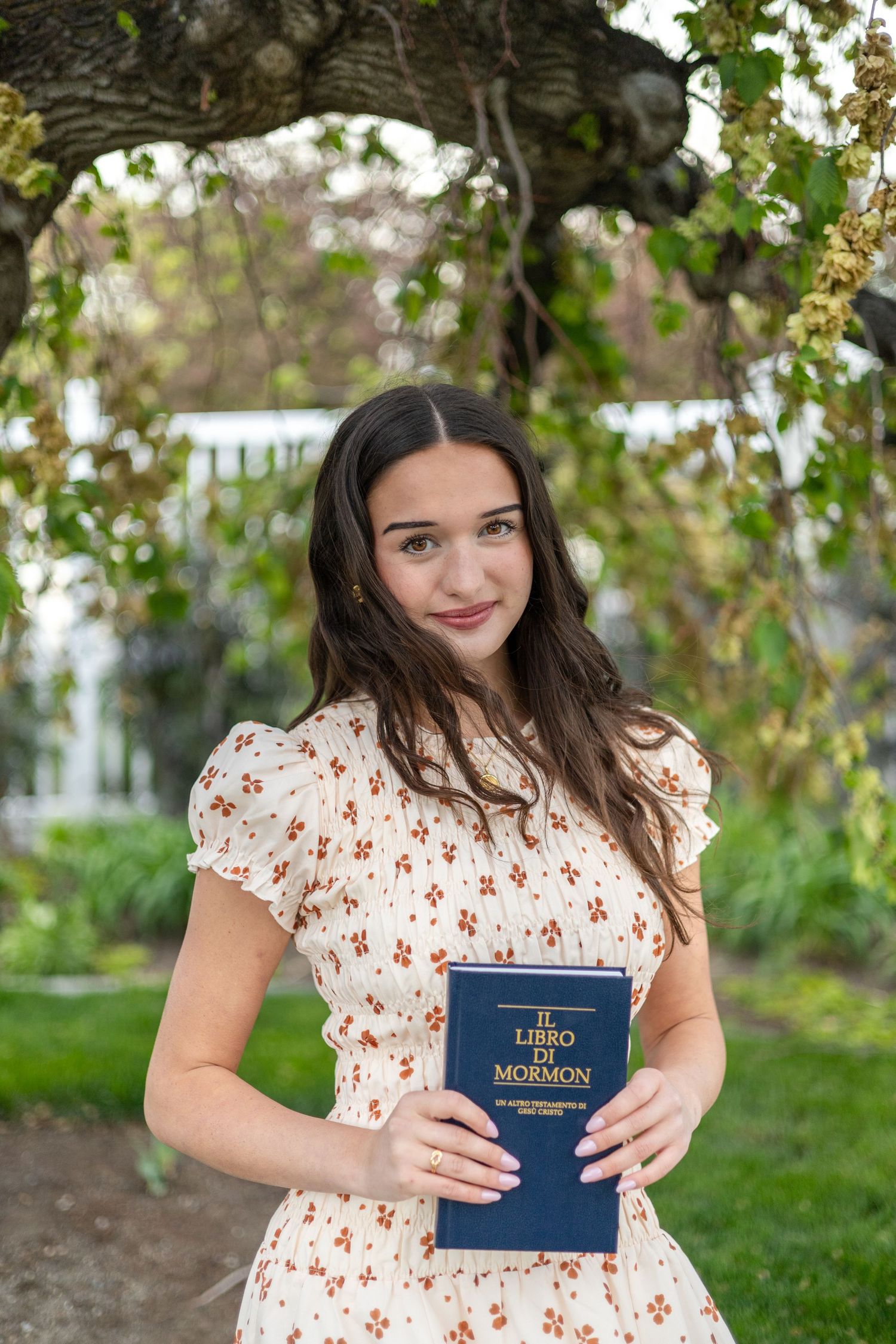 girl holding a book of scripture, posing by a tree at an LDS temple