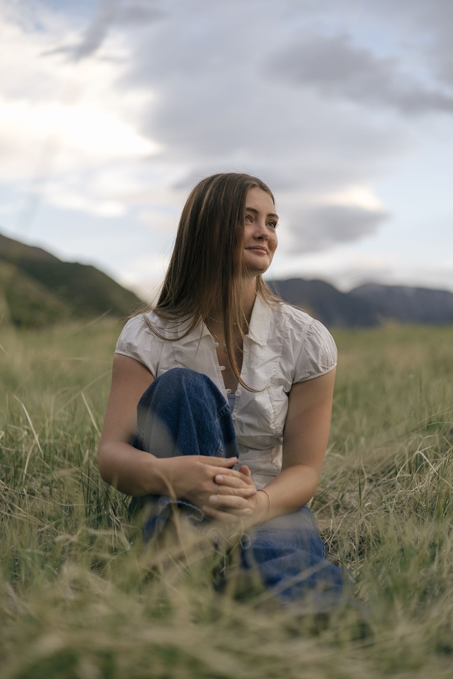 senior girl posing in a field, looking towards the setting sun