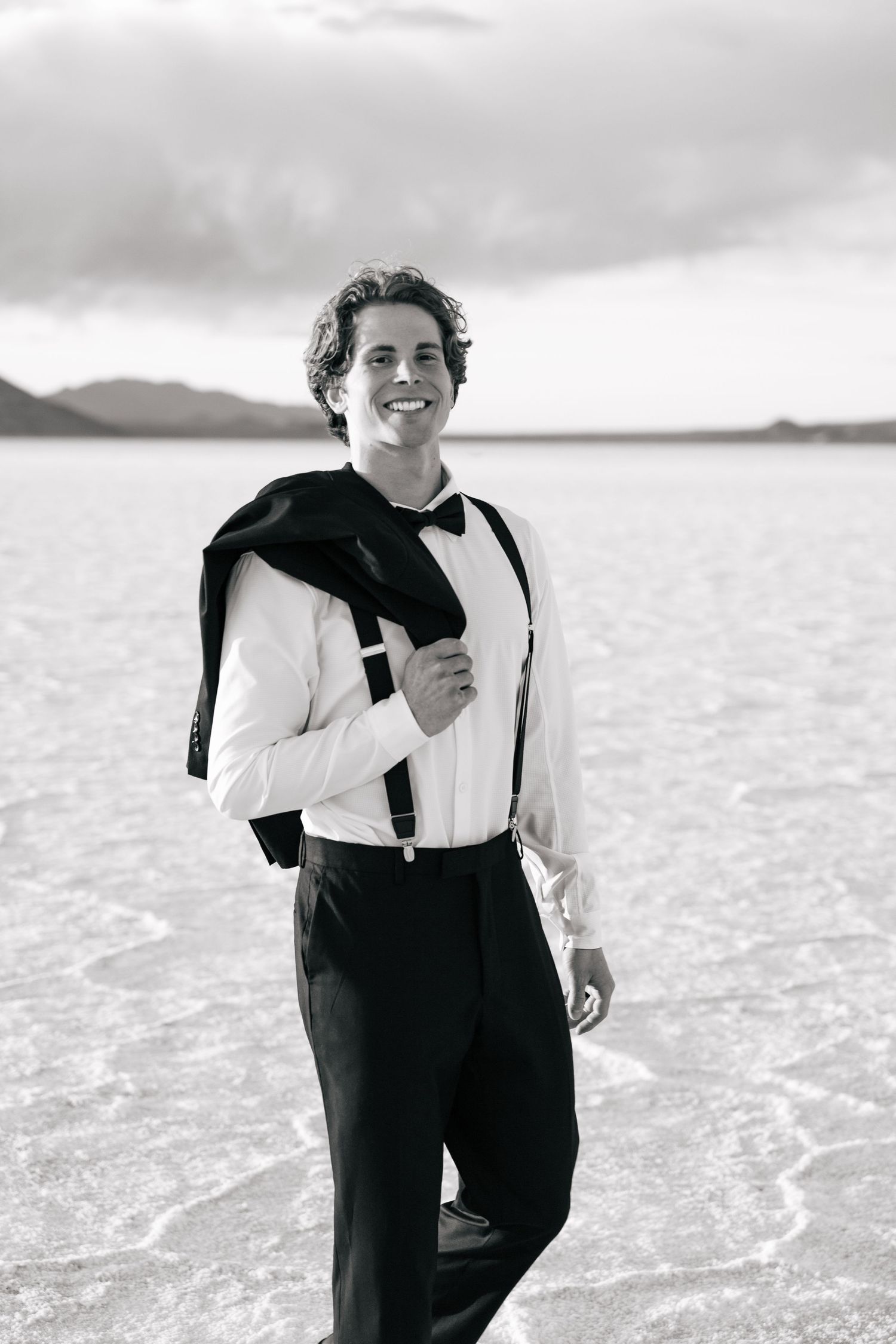 guy at the Utah salt flats with jacket over his shoulder, walking and smiling at camera