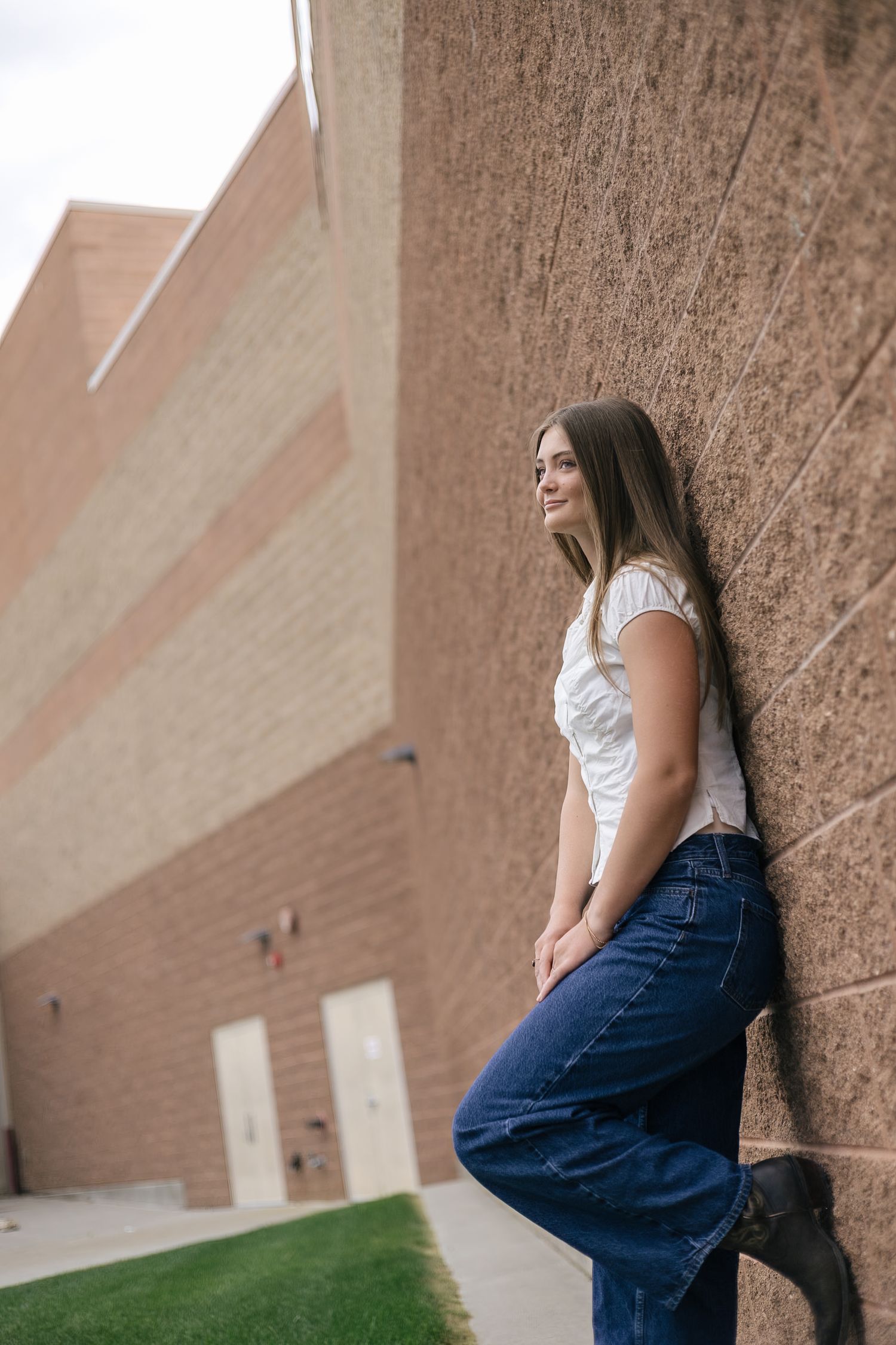 senior girl posing at her school, with foot up against the wall