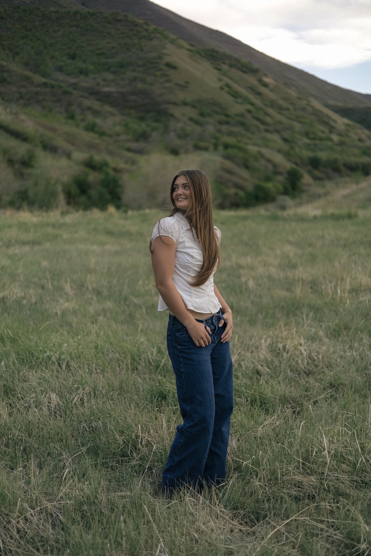 senior girl posing in a field, with thumbs tucked into belt loops