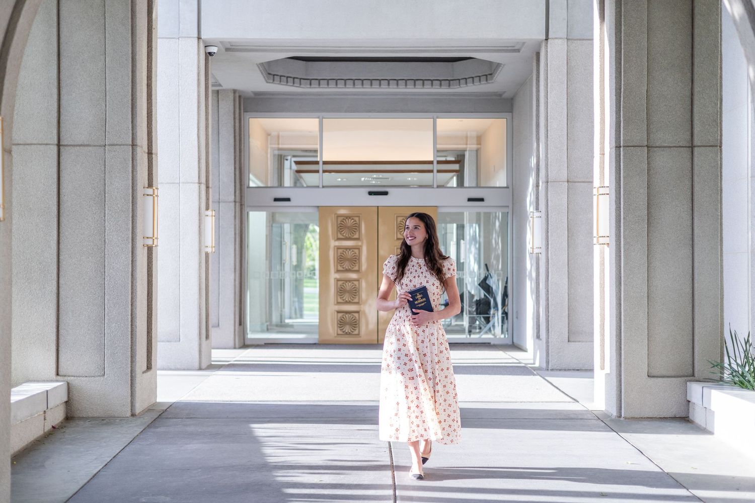 girl holding a book of scripture, walking at an LDS temple