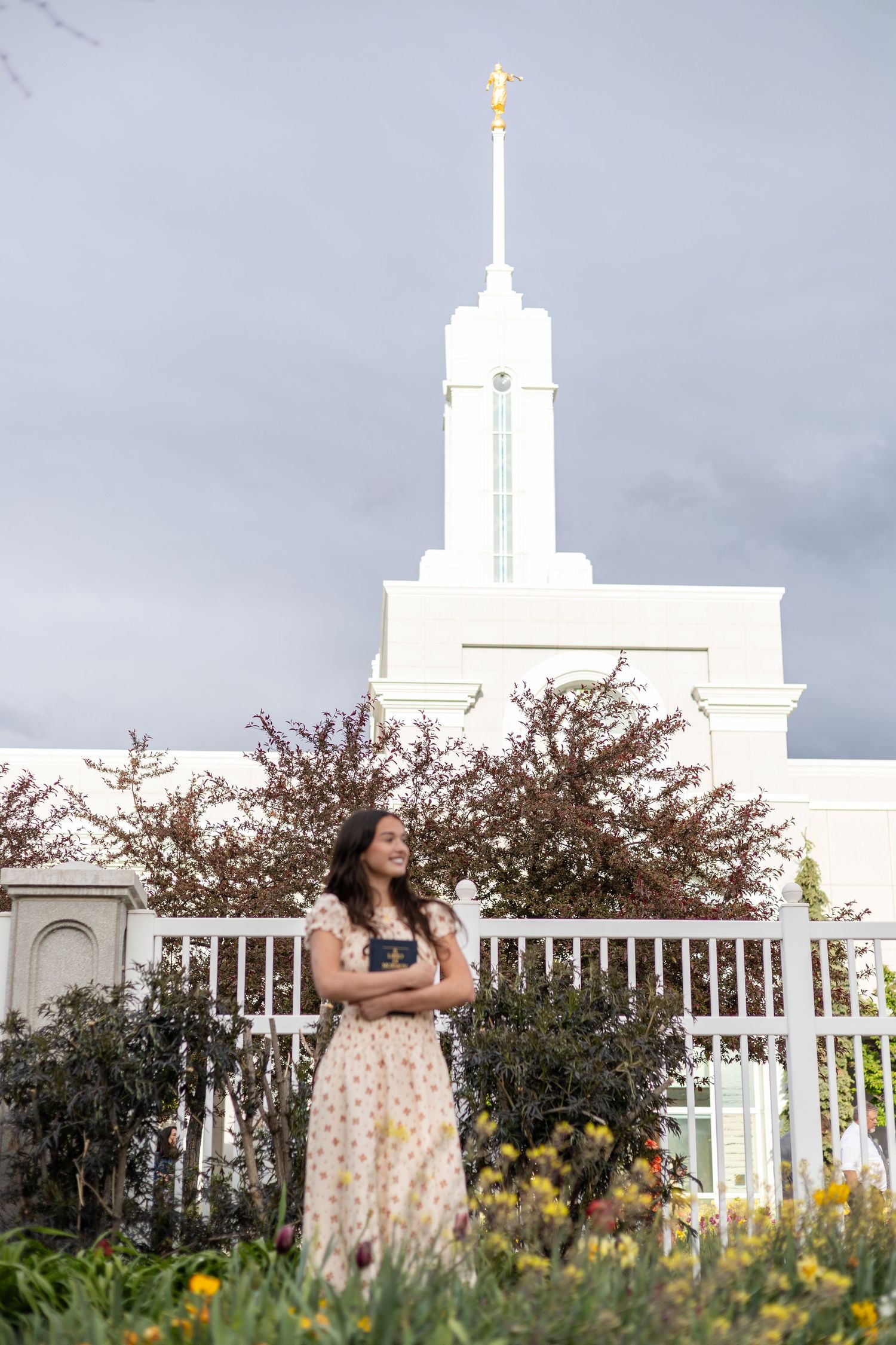 girl holding a book of scripture, posing at an LDS temple gate