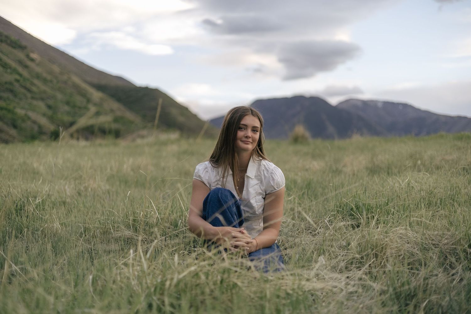 senior girl posing in a field, with arms around bent knee