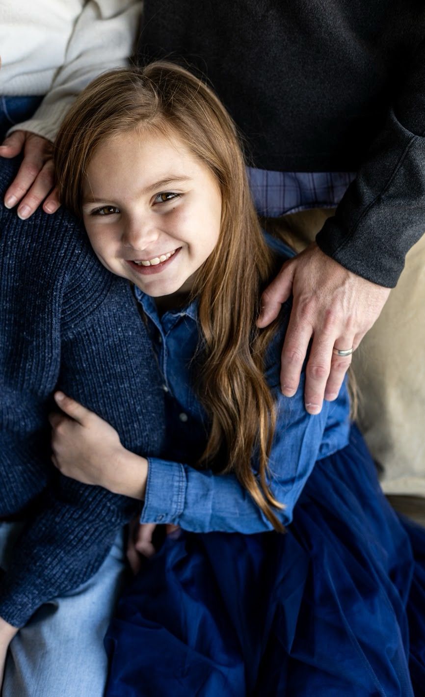 Young person wearing blue denim and navy cardigan smiles while sitting with family members. Cincinnati/ Northern Kentucky