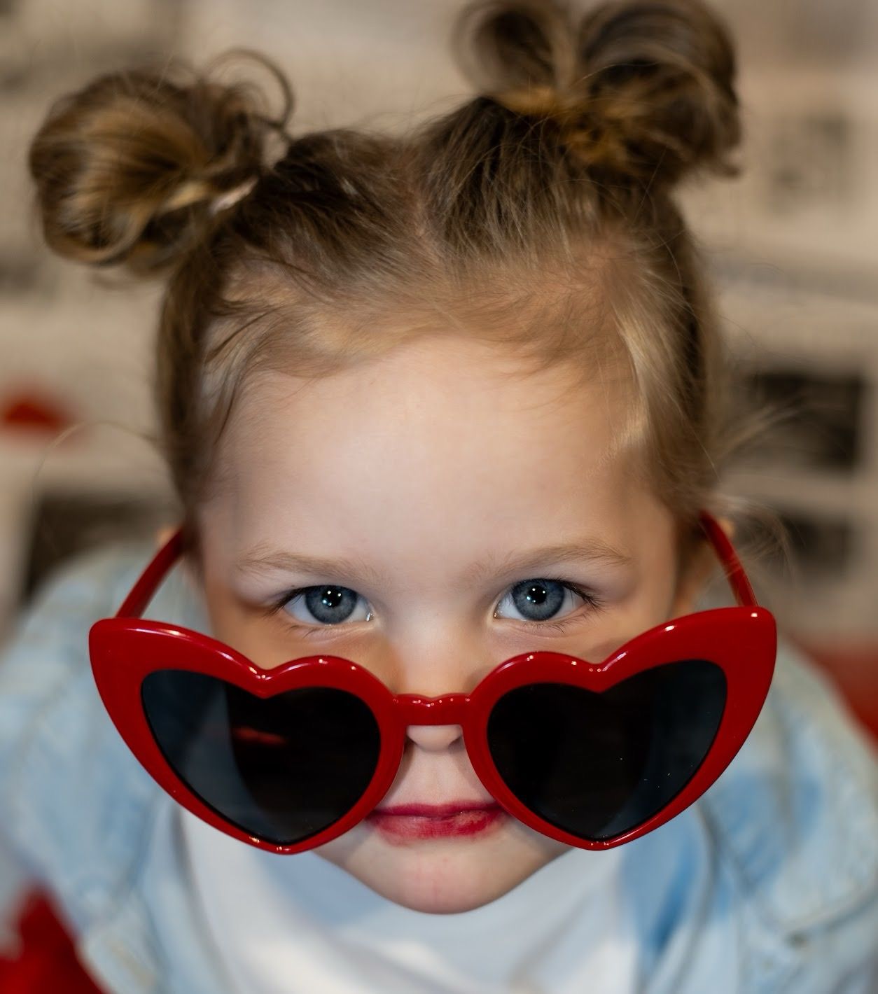 A close-up view of bright blue eyes peeking over red heart-shaped sunglasses in a playful pose. Cincinnati/ northern Kentucky mini session