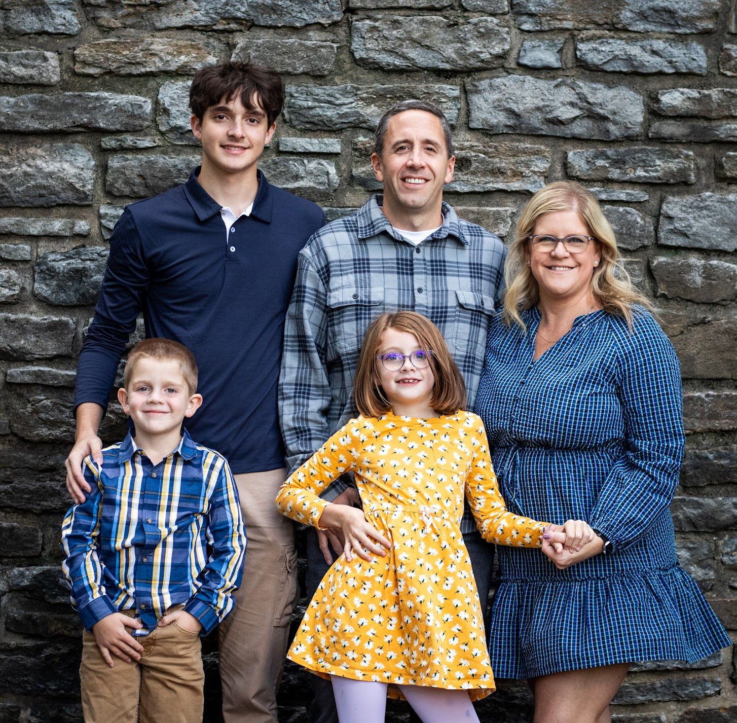 Family portrait session against rustic stone wall backdrop showing casual poses and coordinated blue outfits.