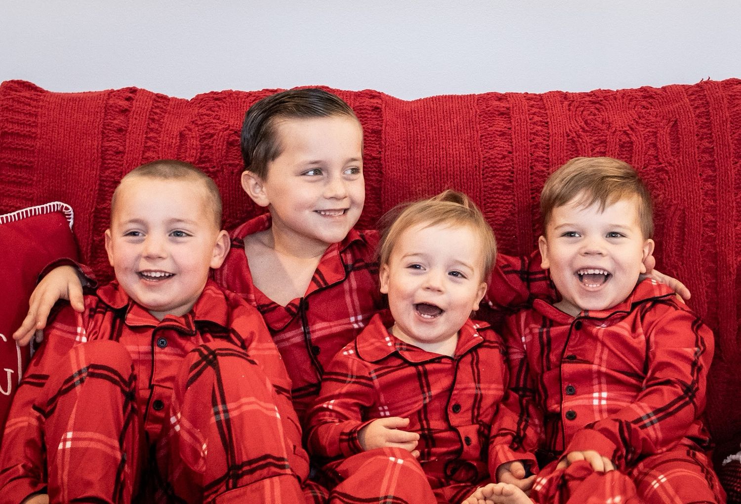 Four children wearing matching red plaid shirts pose together against a red textured backdrop. Cincinnati/ northern Kentucky