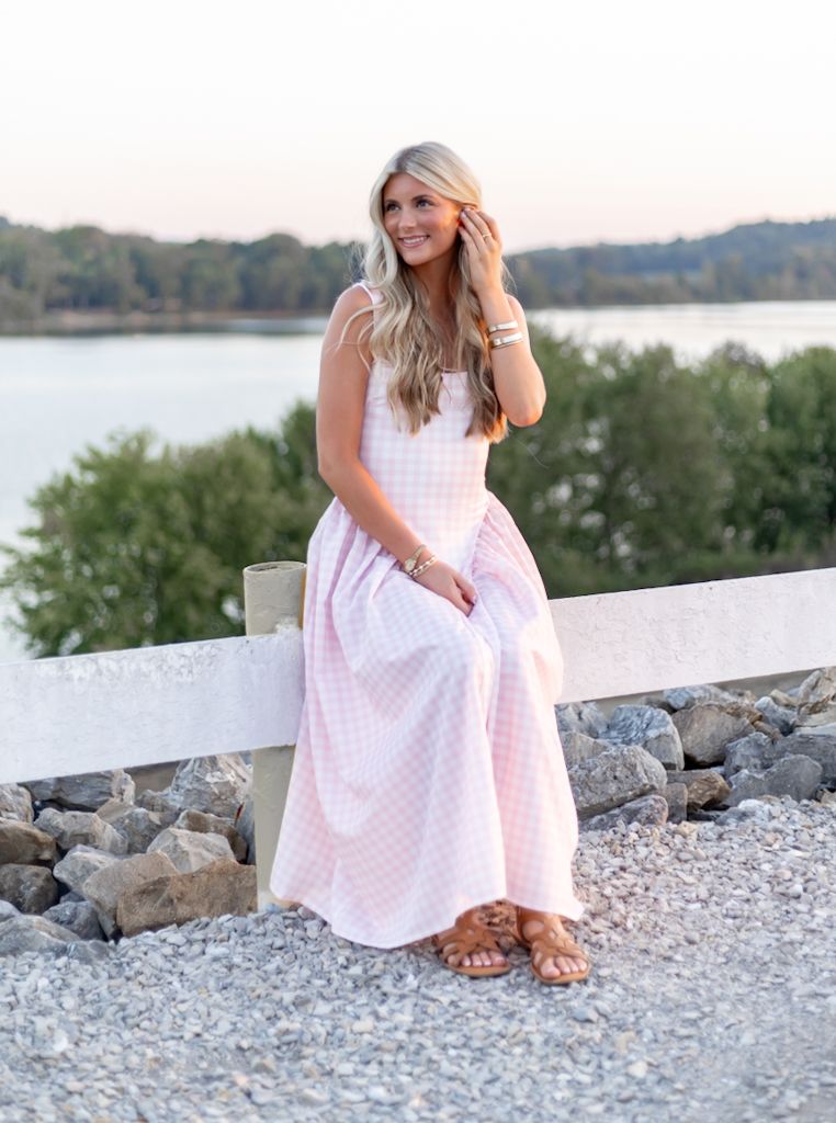 Woman in a pink polka dot dress sits on a rocky shoreline by a lake at sunset. Cincinnati/ northern Kentucky