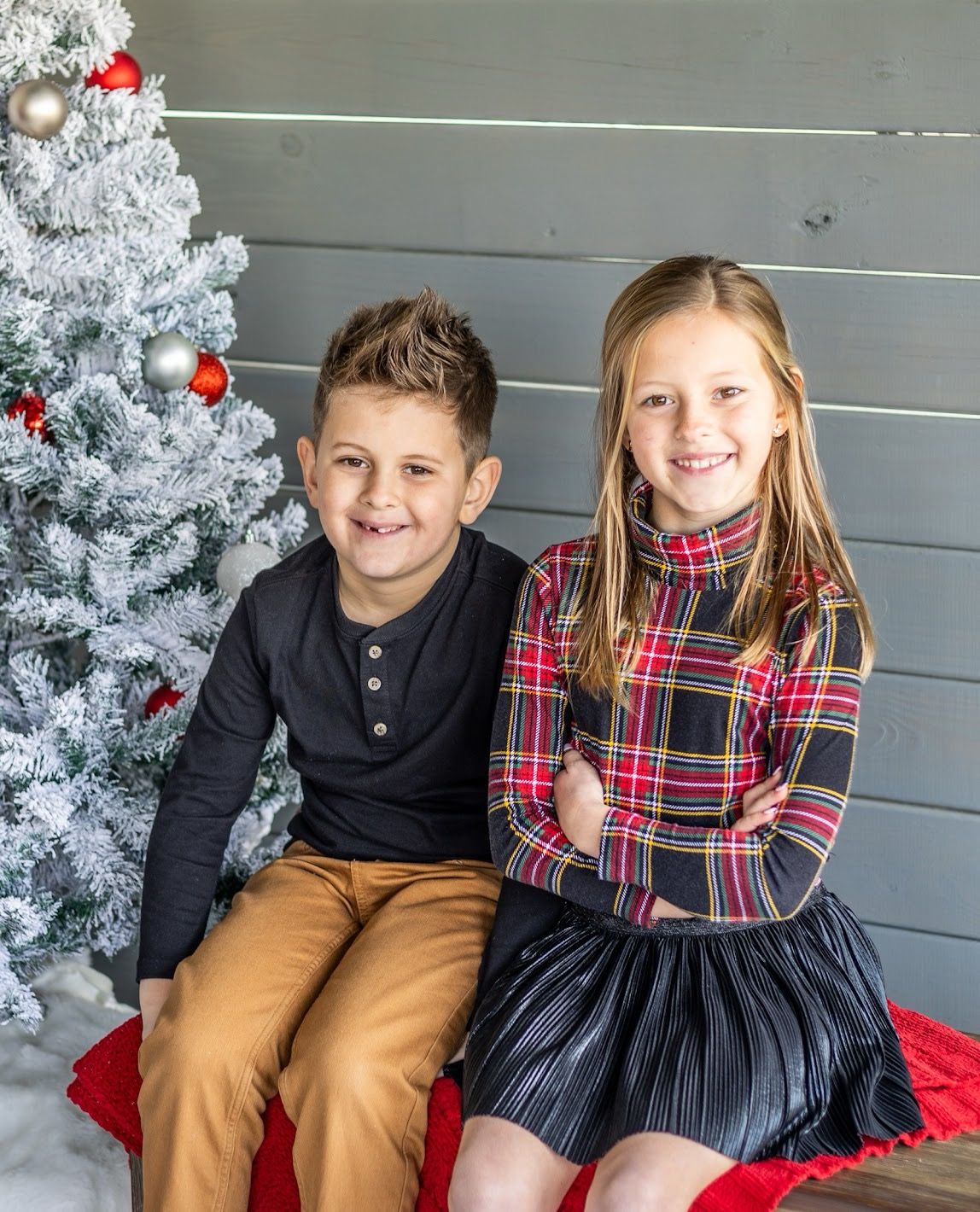 Two children in holiday attire pose together by a white Christmas tree on a red blanket. Serving Cincinnati & Northern Ky