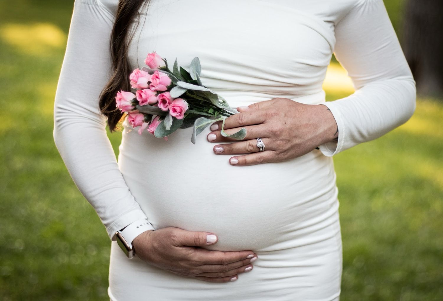 A series of maternity photos showing a pregnant belly in a white dress with pink flowers against a sunny outdoor backdrop. Cincinnati