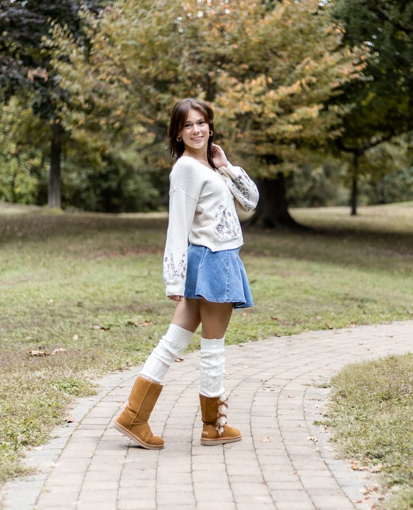 A person in a white sweater and brown boots walks along a curved brick pathway through an autumn landscape. Cincinnati/ northern Kentucky