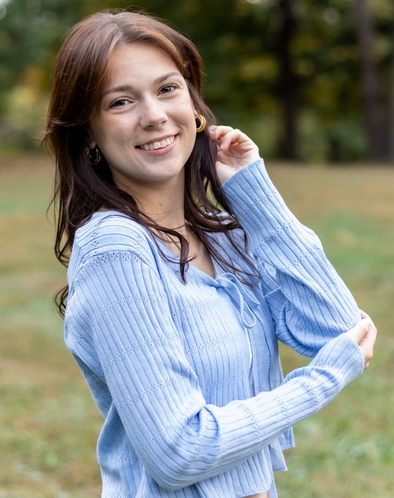 Person wearing a light blue ribbed sweater smiles warmly while posing outdoors in an autumn setting. Cincinnati/ northern Kentucky