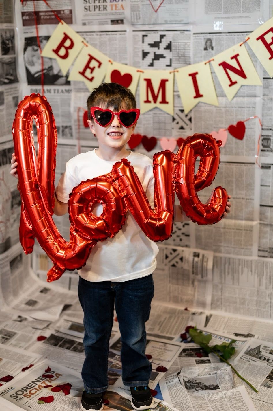 Valentine's Day decorations with red balloon letters and heart decorations arranged on newspaper-covered floor.