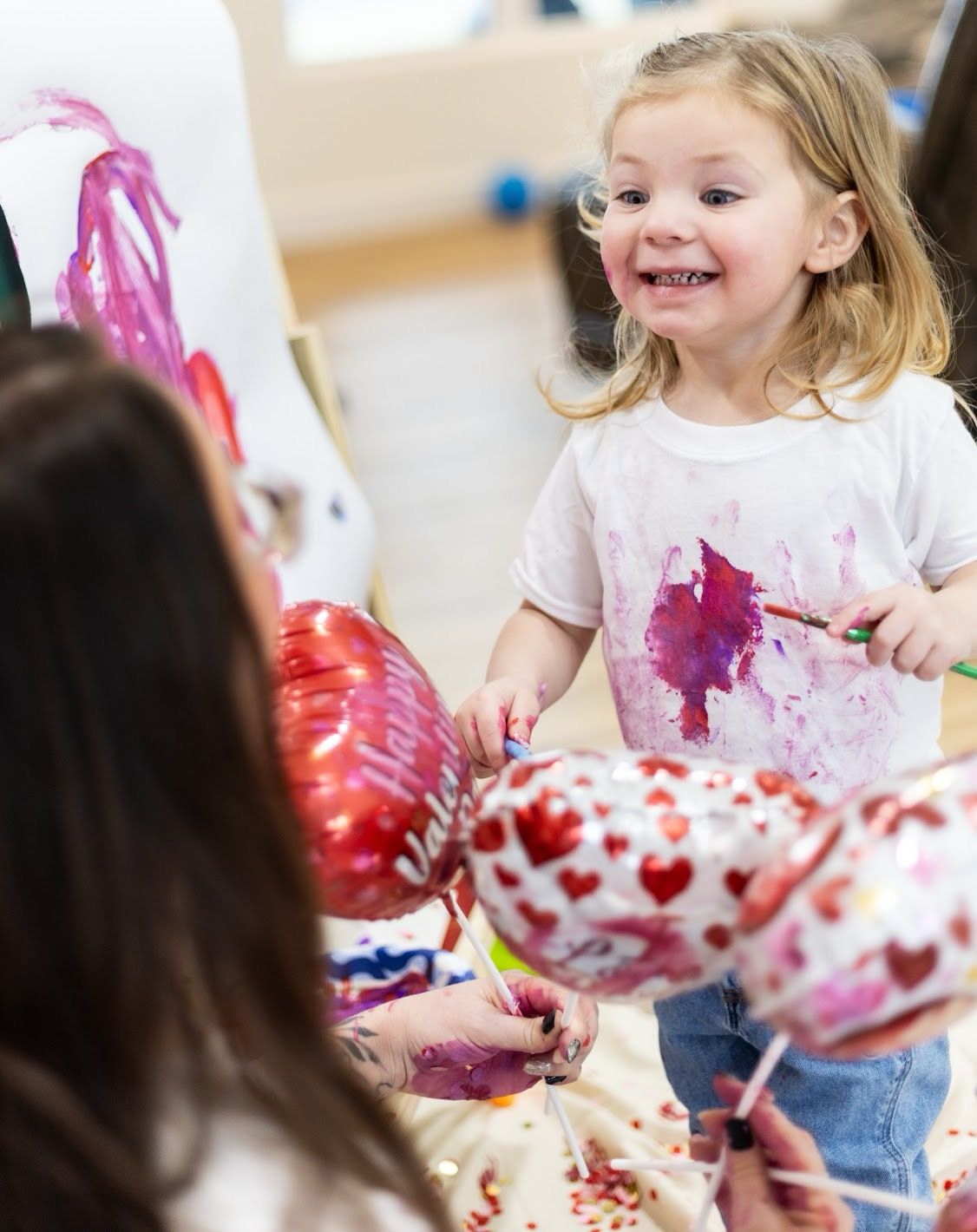 Child in white shirt enjoy messy art activities with pink and red paint during a creative class. Cincinnati/ northern Kentucky