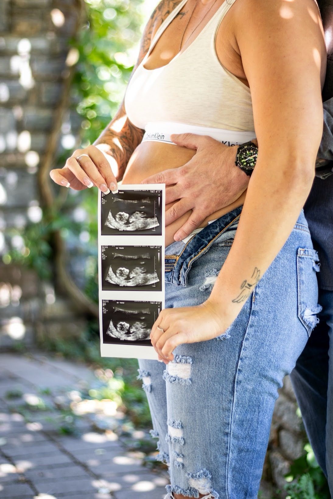 Person in distressed denim jeans holds ultrasound photos while standing outdoors in natural lighting.