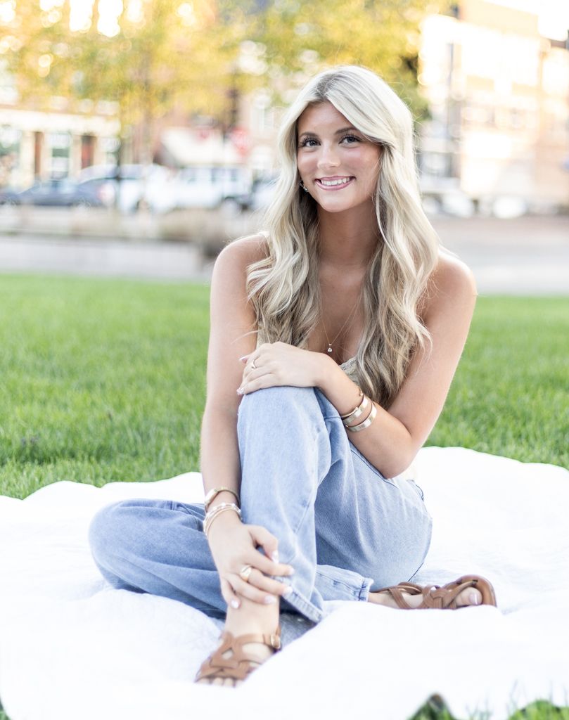 A person in a light blue dress lies on a white blanket on grass during a sunny outdoor photo session. Cincinnati/ northern Kentucky