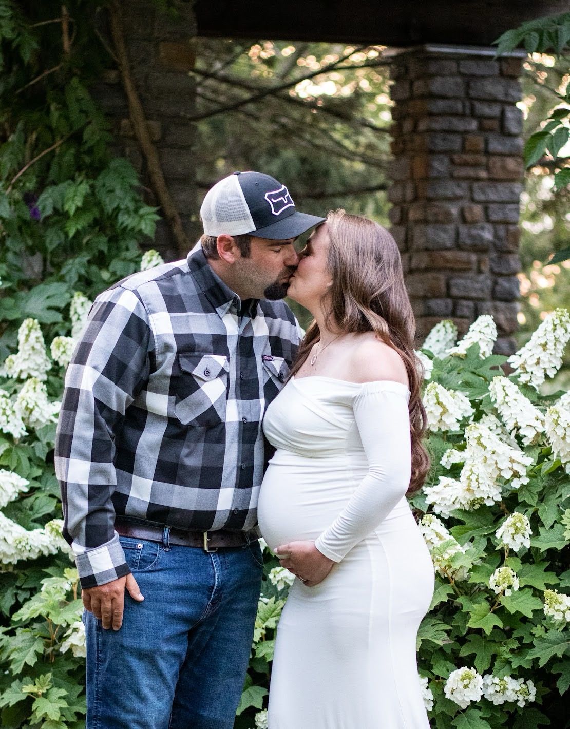 A couple in a rustic outdoor setting with white flowers, wearing matching buffalo plaid and white outfits. Cincinnati/ Northern Kentucky