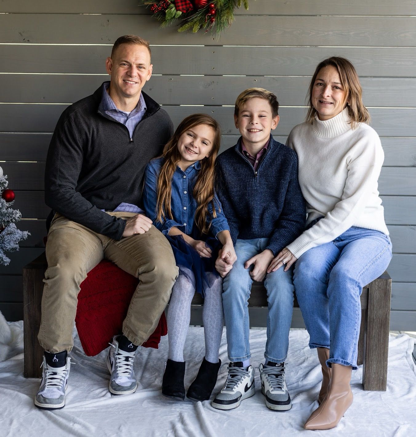 A family sits together on gray porch steps with a festive holiday wreath hanging above them. Cincinnati/ northern Kentucky