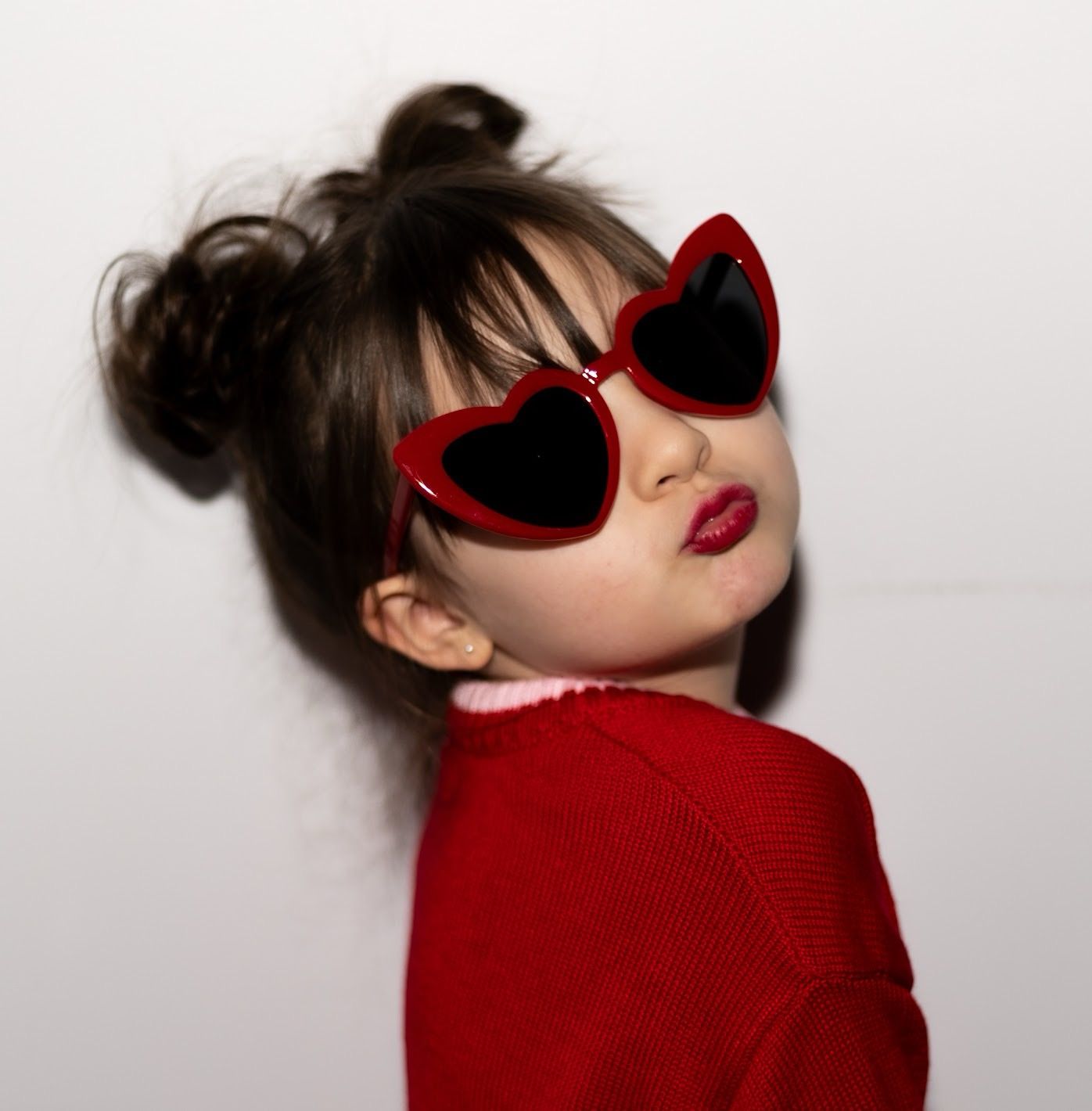 Girl in red sweater and heart-shaped sunglasses poses playfully in a photo collage against white background.