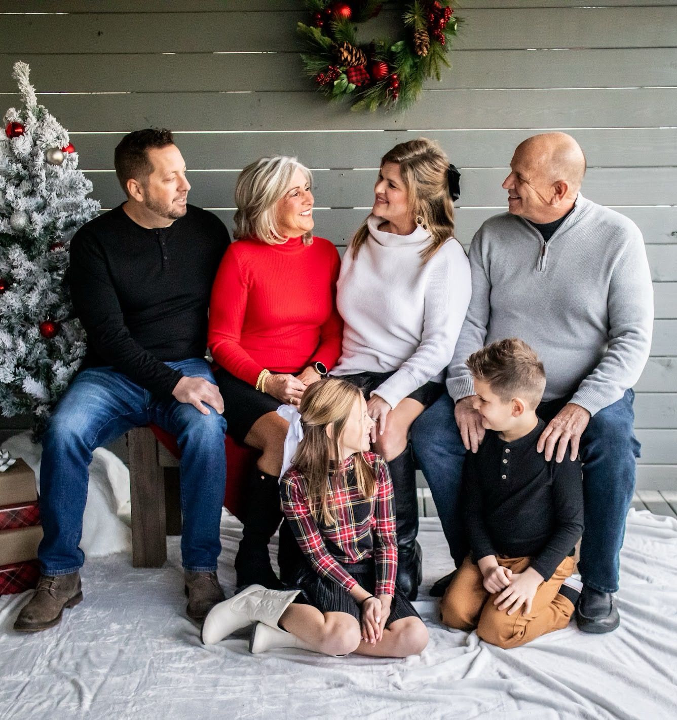 Family sitting together on a porch bench with holiday wreath and festive Christmas decorations in the background.