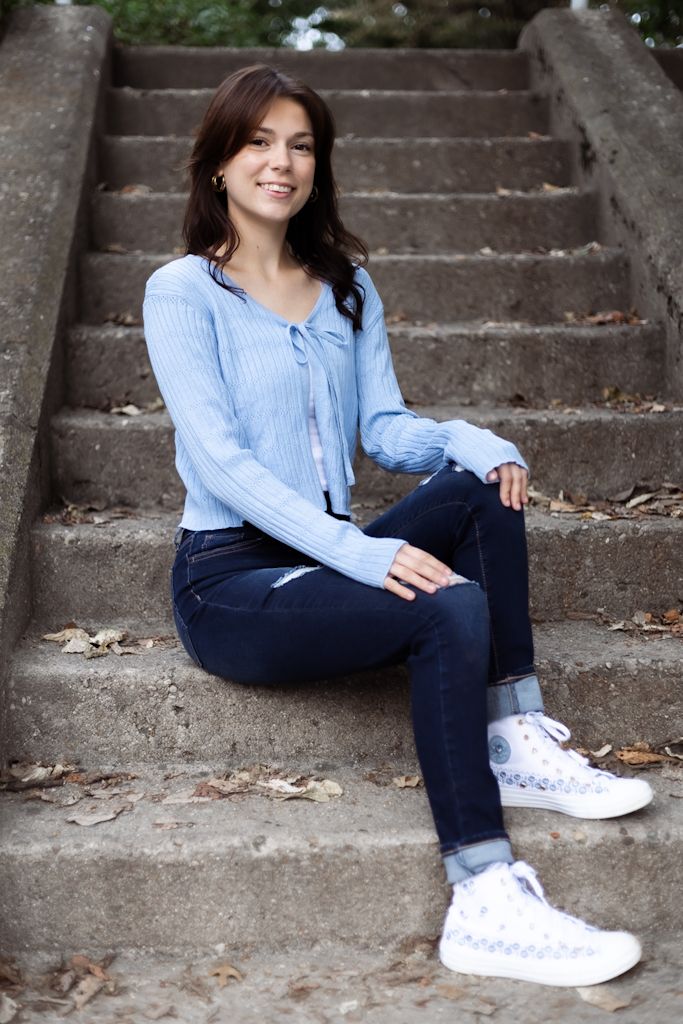 A casual portrait on concrete steps featuring a light blue sweater, dark jeans, and white sneakers. Cincinnati/ northern Kentucky