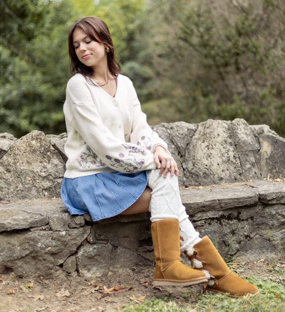 Person in white blouse and jeans sitting on stone wall wearing brown boots in outdoor natural setting. Cincinnati/ northern Kentucky
