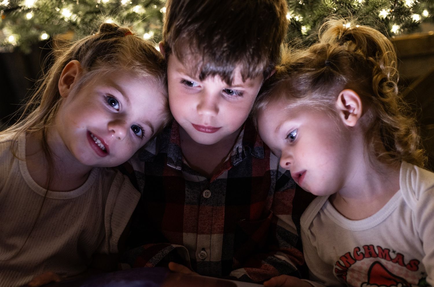 Siblings reading a book together in front of Christmas tree. Cincinnati/ northern Kentucky