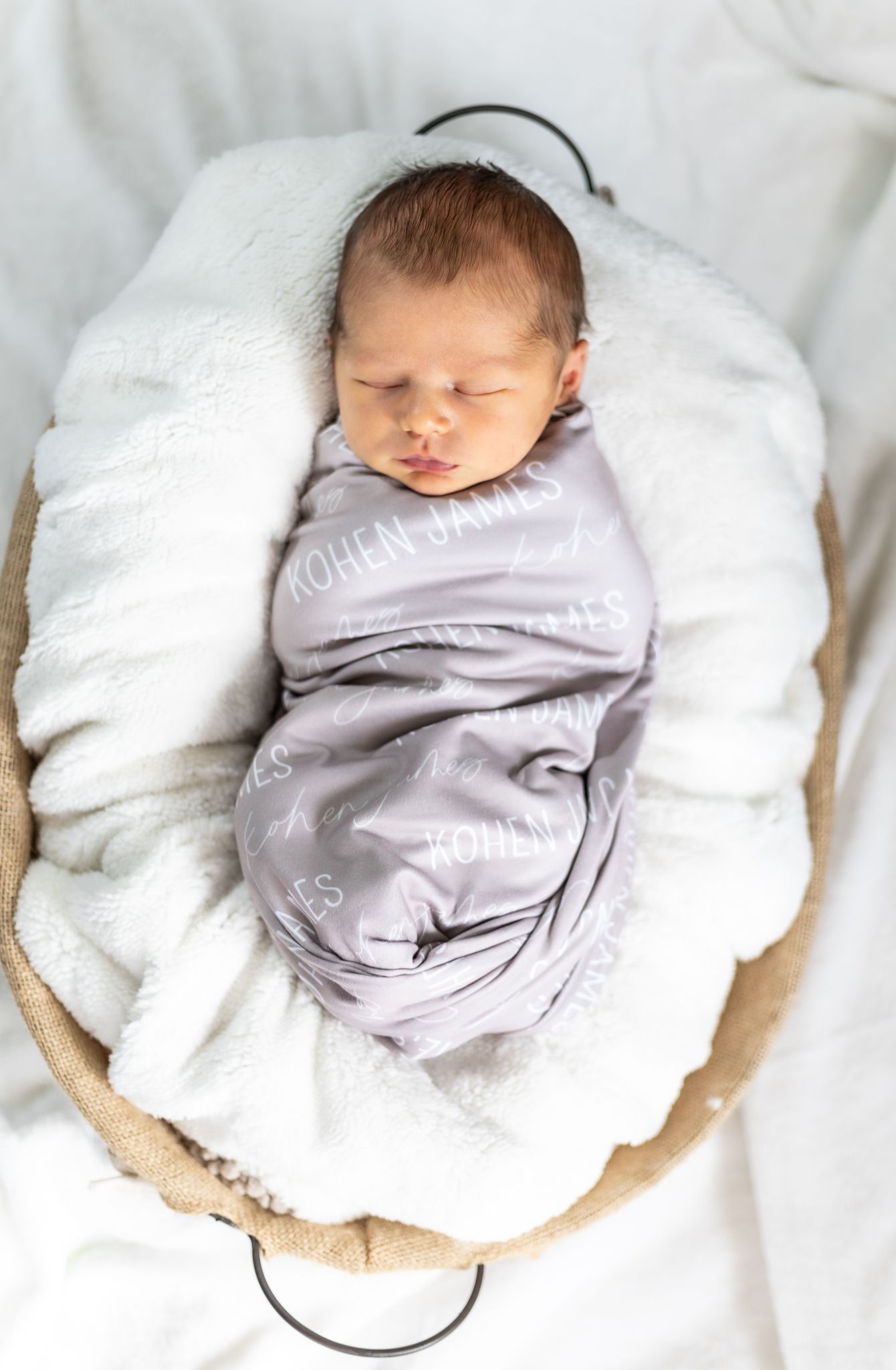 A sleeping baby wearing grey clothing rests peacefully on white bedding. Cincinnati/ Northern Kentucky