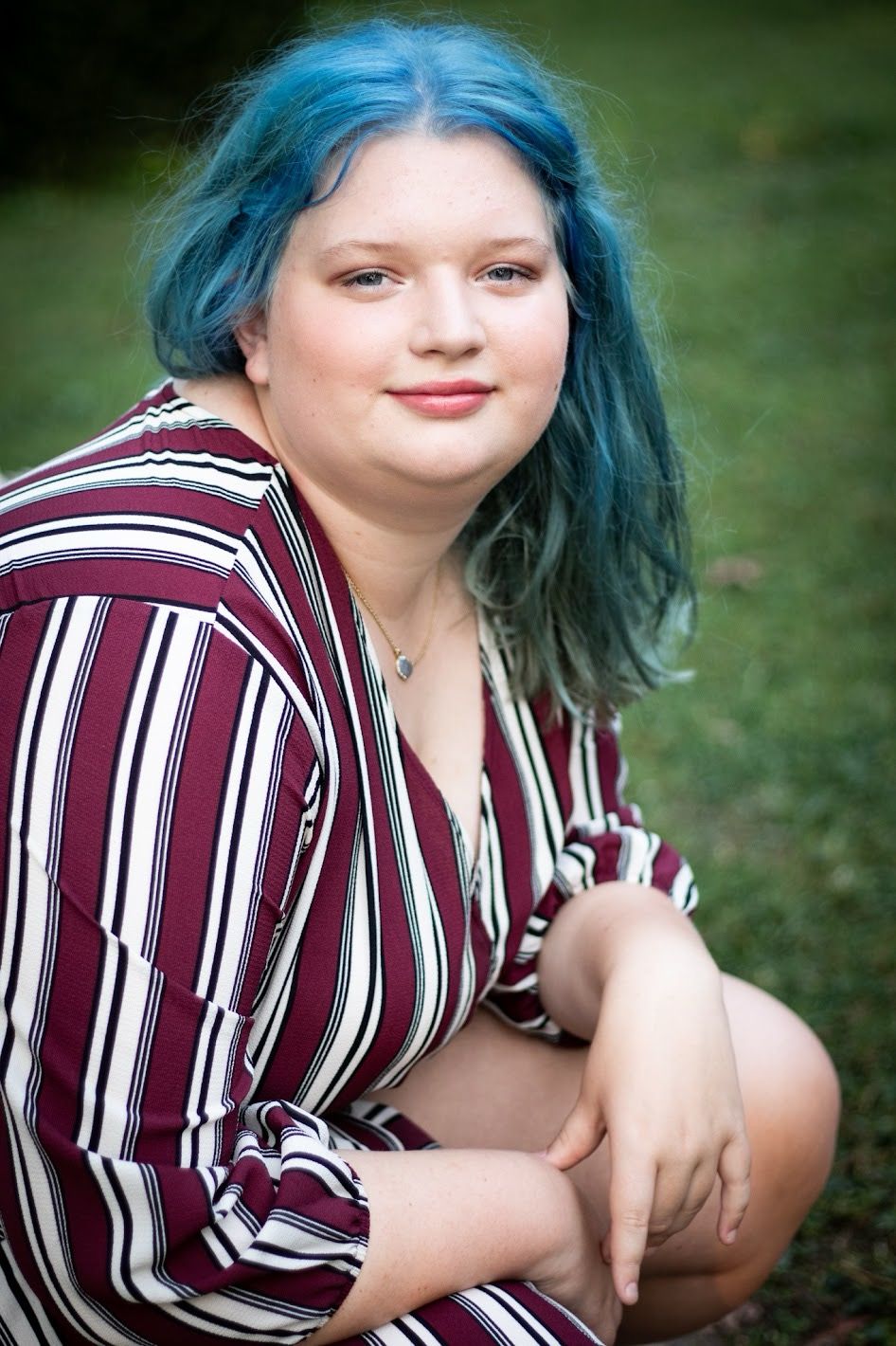 A person in a burgundy striped dress poses in front of a stone wall with green foliage in the background. Female senior Cincinnati/