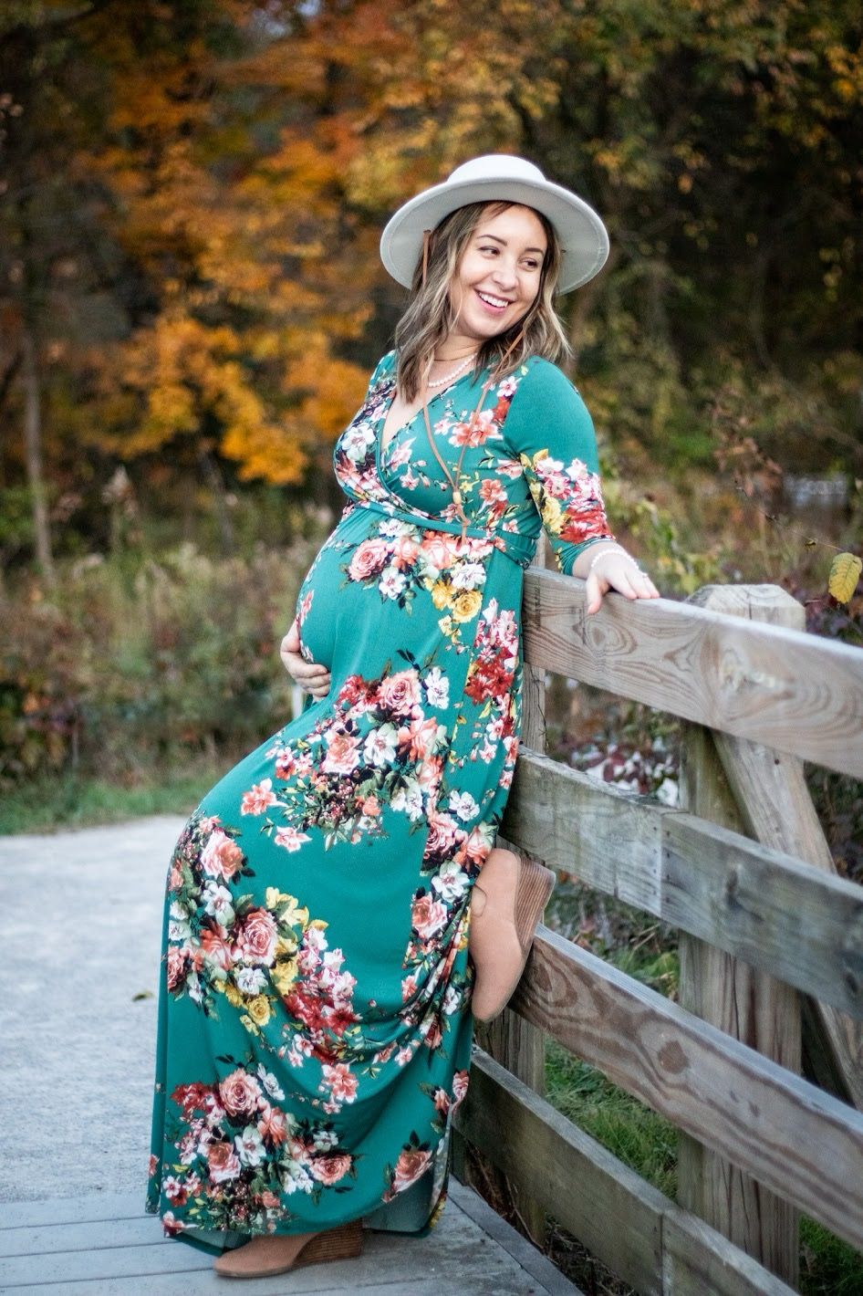 Woman in green floral dress and gray hat poses on wooden bridge during autumn season. Cincinnati Nature Center